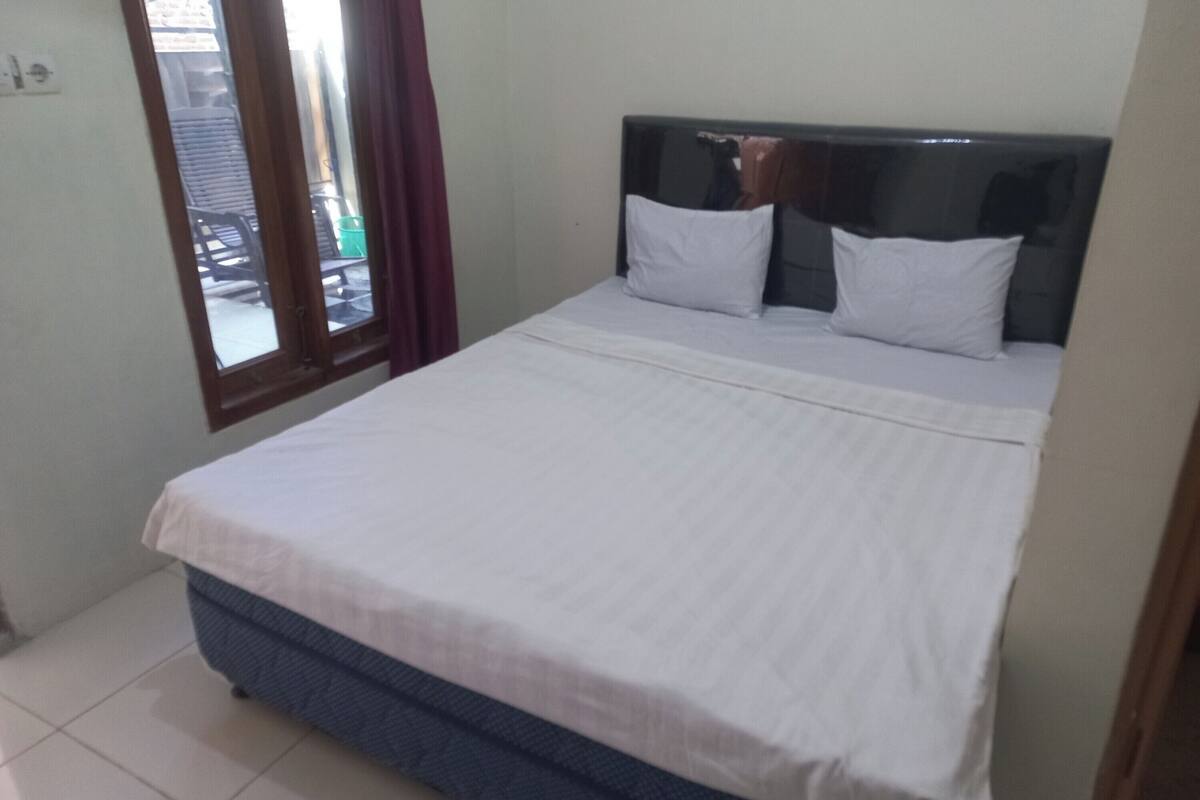 Un lit simple avec une tête de lit, du linge de lit blanc et une fenêtre avec des rideaux.
