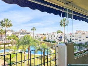 A balcony with a view of a swimming pool, palm trees, and residential buildings.