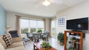 A living room with a sofa, coffee table, TV stand, and dining area with chairs and a table. - Gulfview II 611 Premier location, Great SpaceX View, Near beach (South Padre Island)