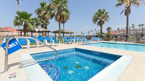A swimming pool with blue tiles, surrounded by lounge chairs and palm trees. - Gulfview II 611 Premier location, Great SpaceX View, Near beach (South Padre Island)