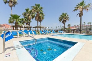 A swimming pool with blue tiles, surrounded by lounge chairs and palm trees.