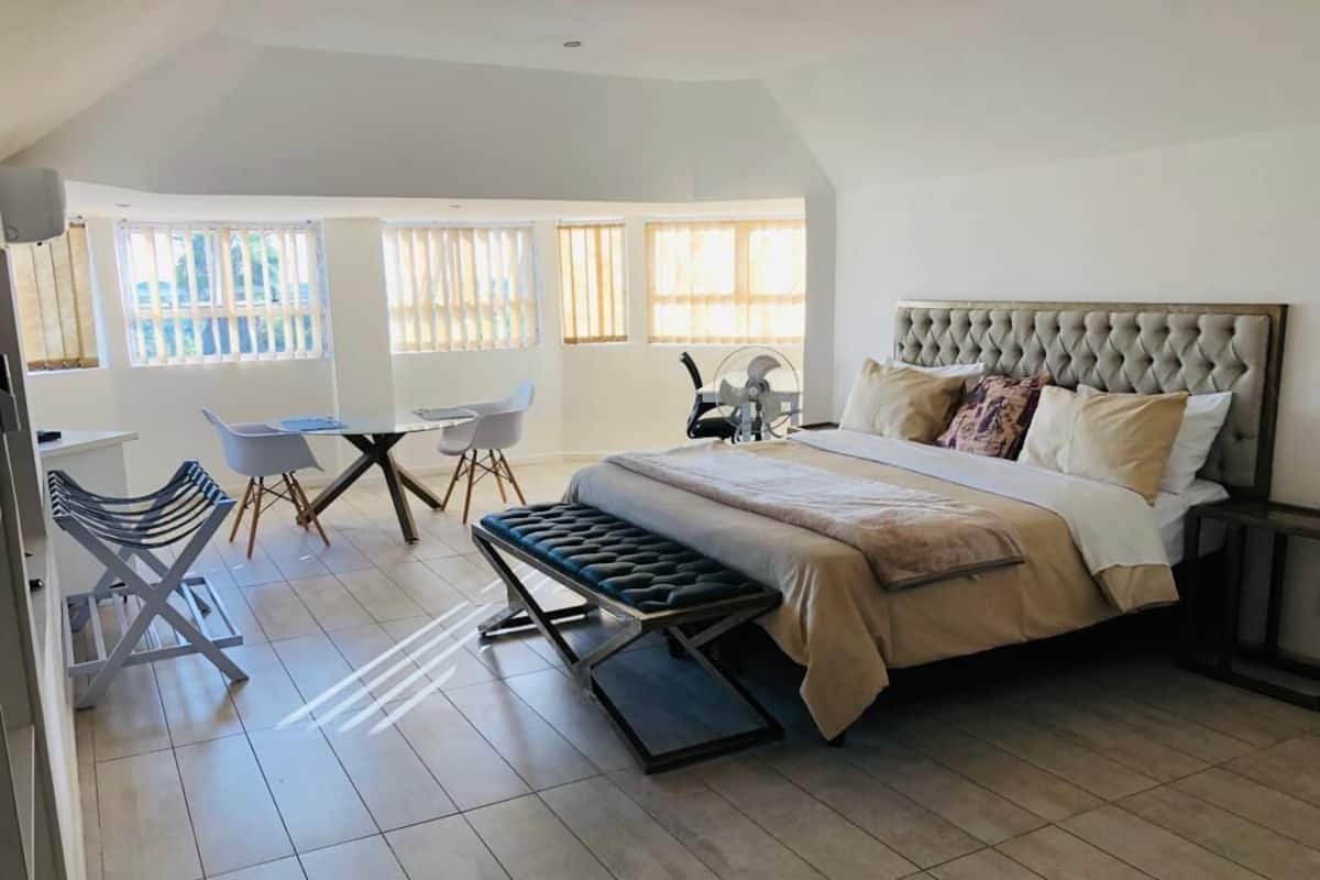 Quarto com uma cama grande, um banco, uma escrivaninha e cadeiras.