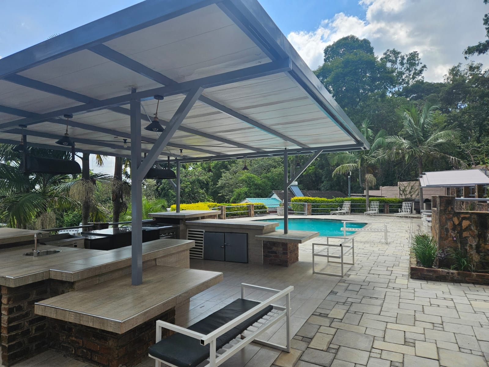 Un espace extérieur avec piscine, comprenant un coin salon couvert, un barbecue et un chemin en pierre.