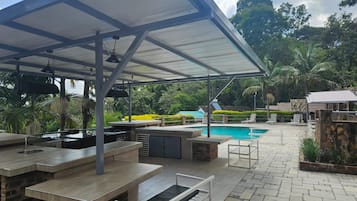 Un espace extérieur avec piscine, comprenant un coin salon couvert, un barbecue et un chemin en pierre.