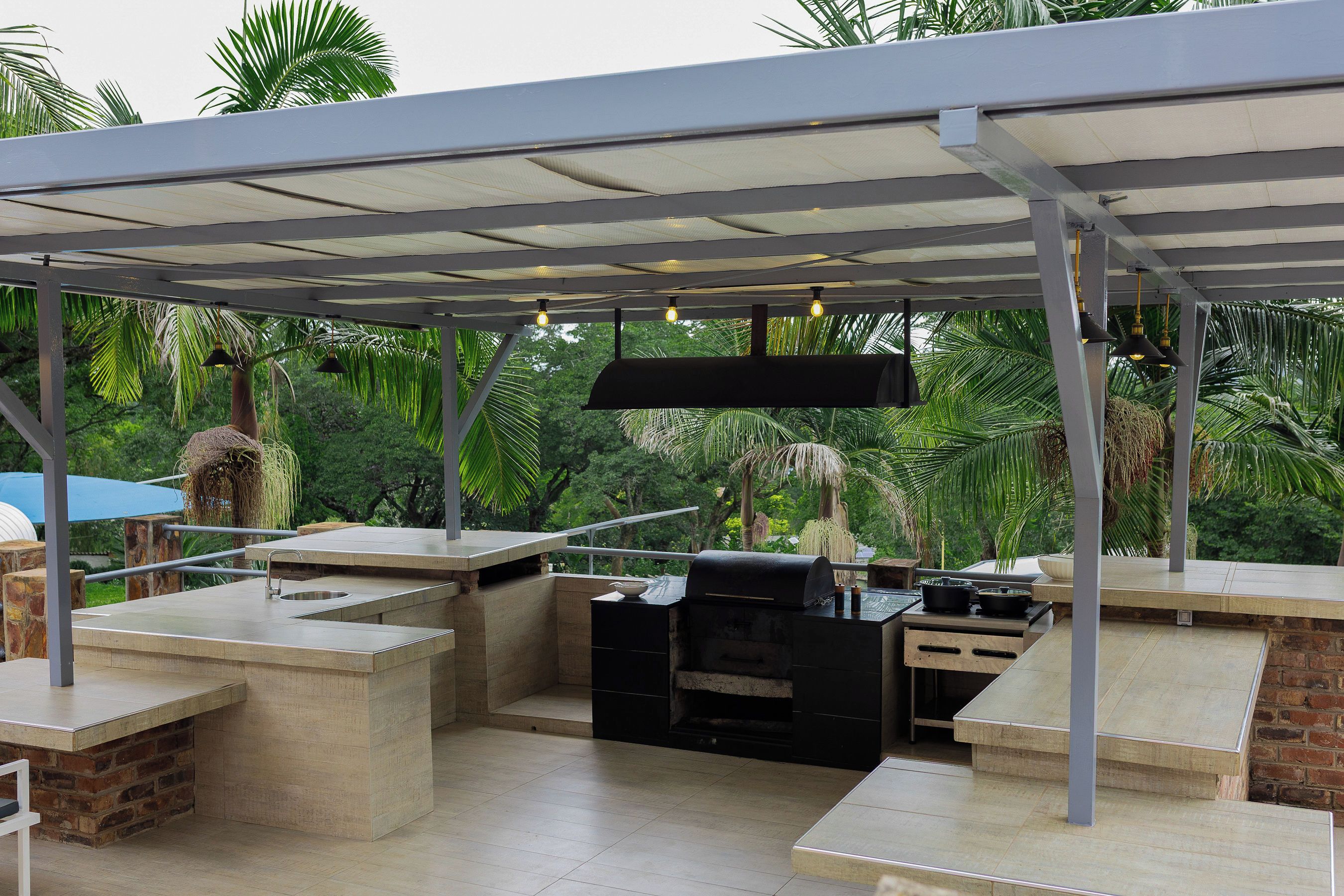 Patio esterno con barbecue, area salotto e spazio coperto con luci a sospensione.