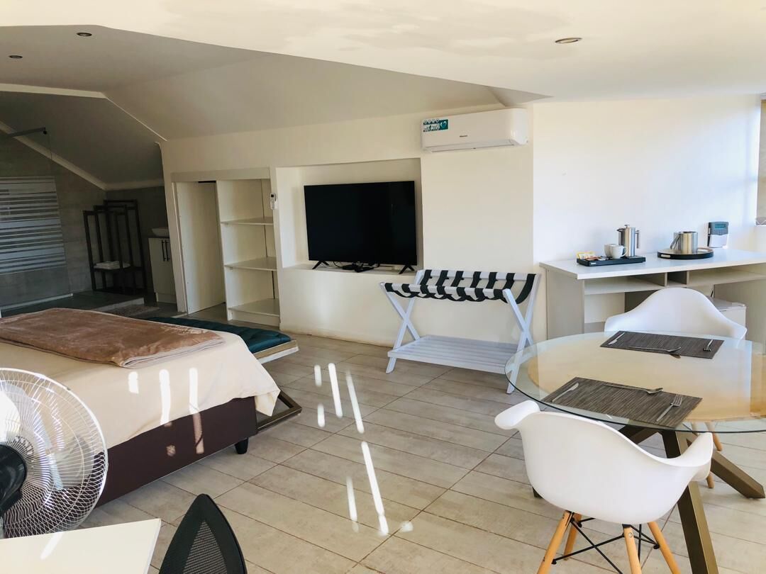 Una habitación de hotel moderna con cama, televisor, zona de estar con mesa y sillas, y una escalera.