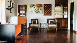 A spacious living room with a dark wood floor, two armchairs, a small table, and a cabinet with glassware. - The Hilltop Guesthouse (Harare)