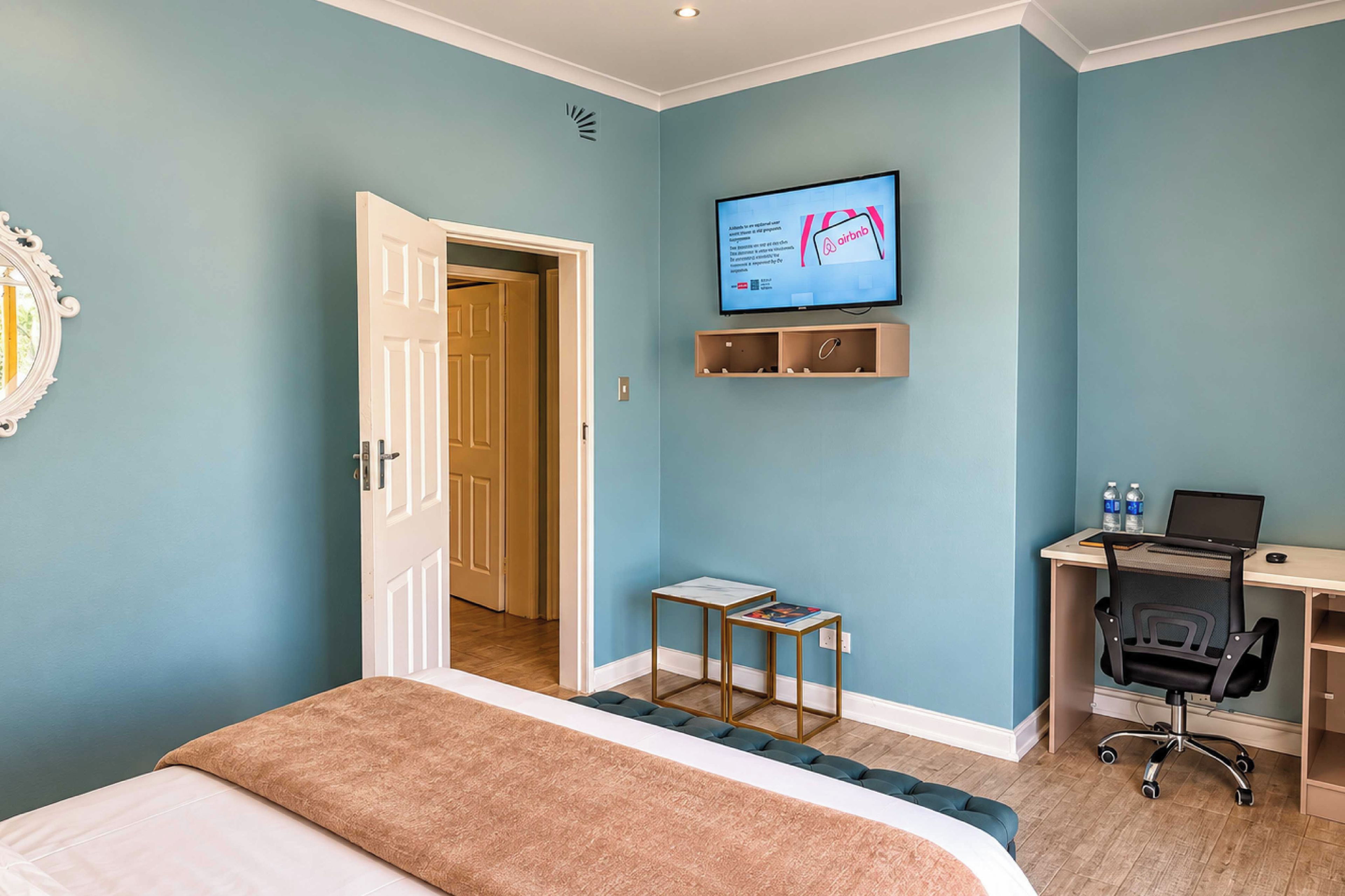 Habitación de hotel con cama, escritorio con computadora portátil, televisor en la pared y puerta que da a otra habitación.