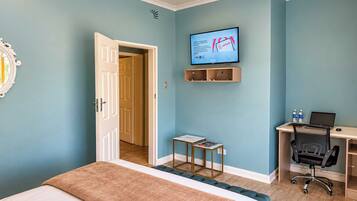 Habitación de hotel con cama, escritorio con computadora portátil, televisor en la pared y puerta que da a otra habitación.