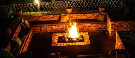 An outdoor fire pit area with brick seating and a wooden fence.