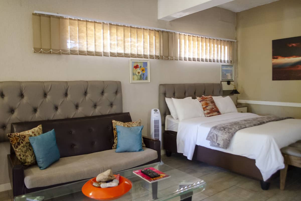Quarto de hotel com sofá, cama, mesa de cabeceira com abajur e janela com persianas.