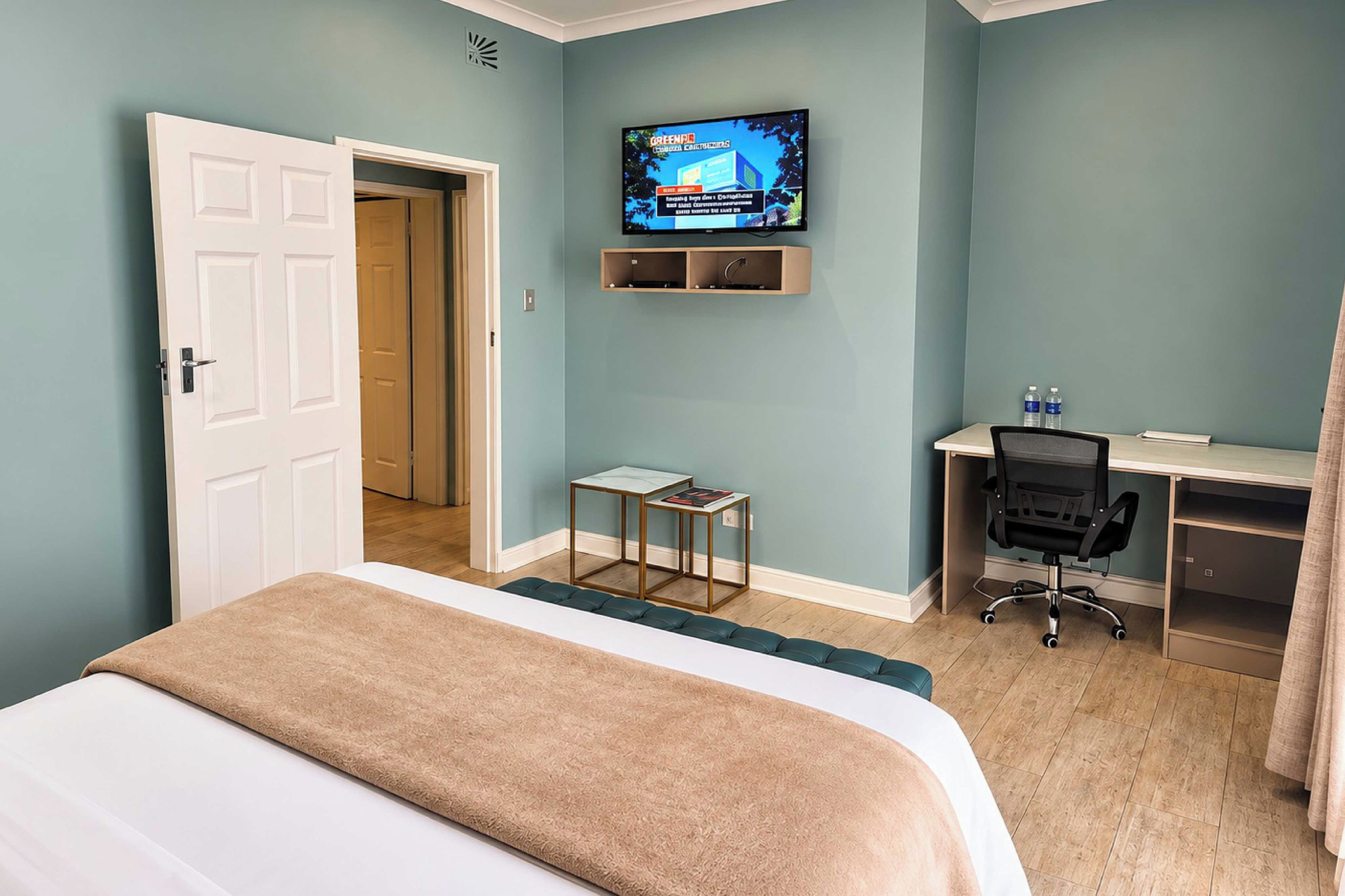 A hotel room with a bed, a desk, a chair, a television, and a small table.