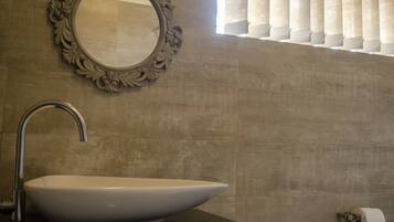 A bathroom with a large oval sink, a wall-mounted mirror with an ornate frame, and a toilet paper holder.
