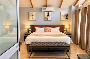 Una habitación de hotel con una cama grande, mesitas de noche con lámparas, un banco y obras de arte en las paredes.