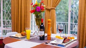 A dining table with a bottle of wine, a glass of orange juice, a vase of flowers, and plates of food. - The Hilltop Guesthouse (Harare)