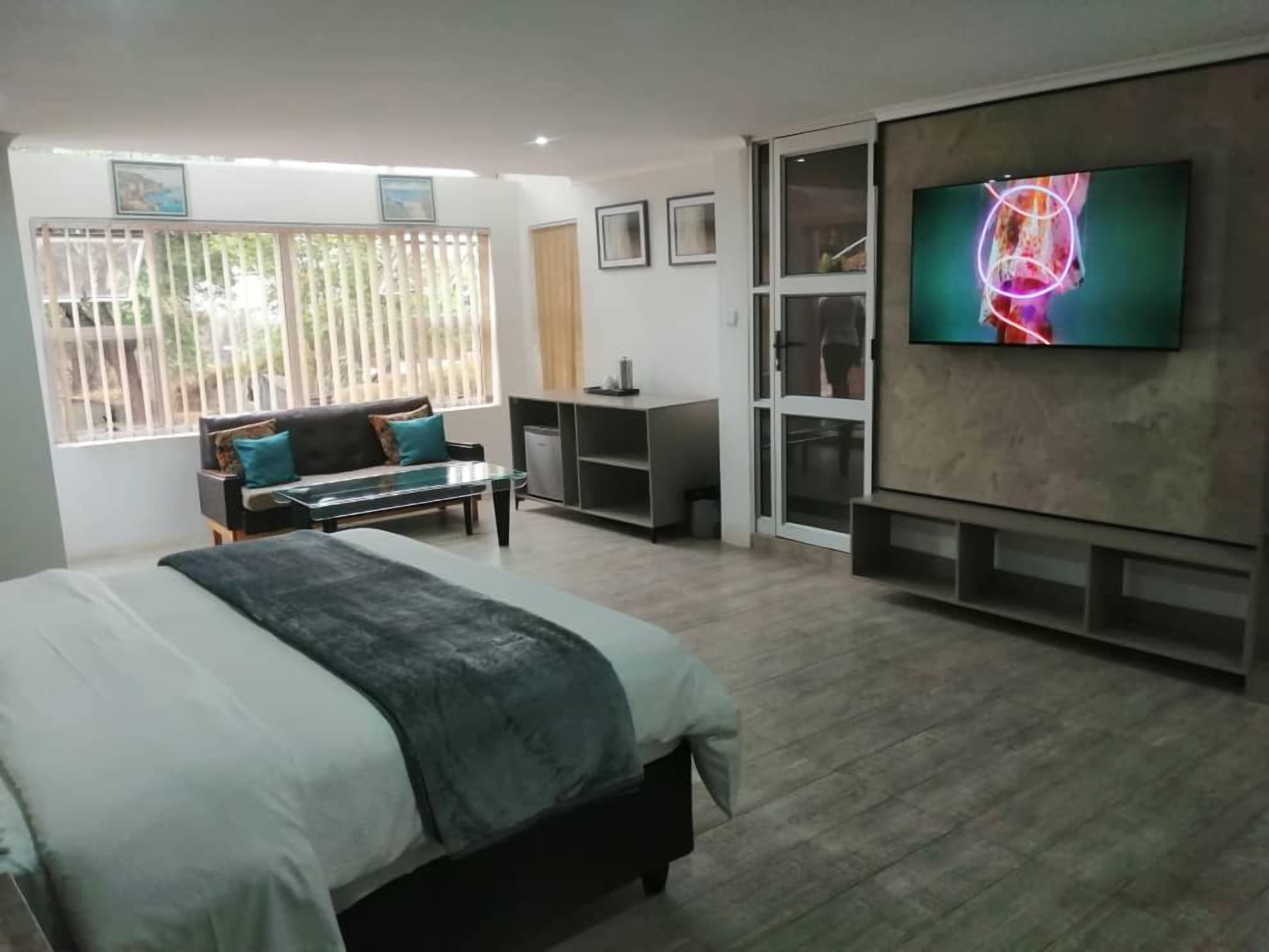 A modern bedroom with a bed, a TV, a sofa, and a desk.