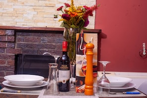Una mesa de comedor dispuesta con platos, una botella de vino, una copa y un florero decorativo con flores.