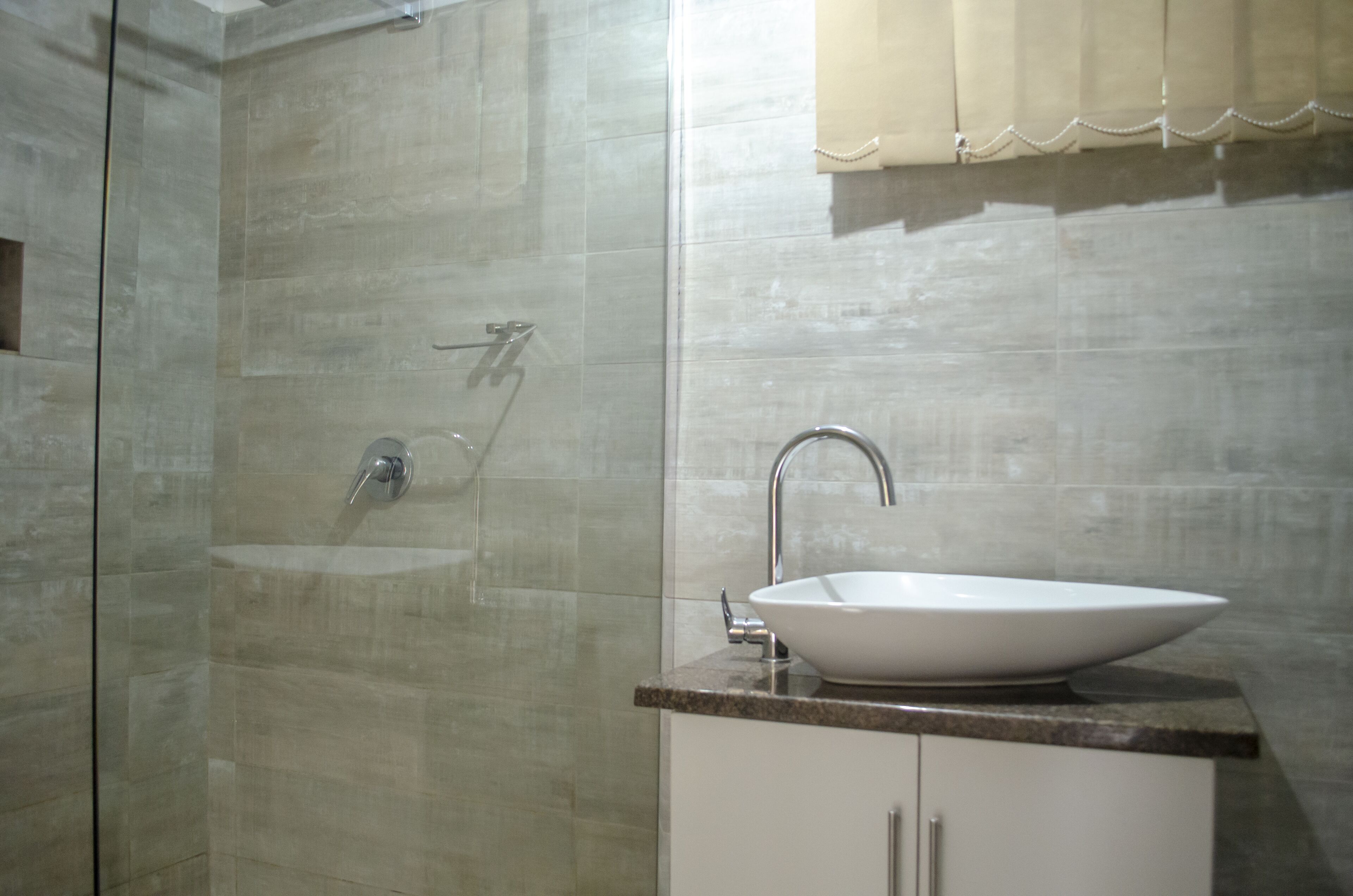 Un baño con ducha separada por vidrio, lavamanos blanco y cortina color beige.