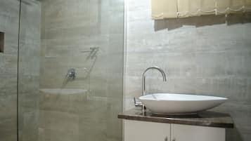 Un baño con ducha separada por vidrio, lavamanos blanco y cortina color beige.