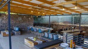 An outdoor patio with wooden tables, blue chairs, and a stone wall backdrop. - The Hilltop Guesthouse (Harare)