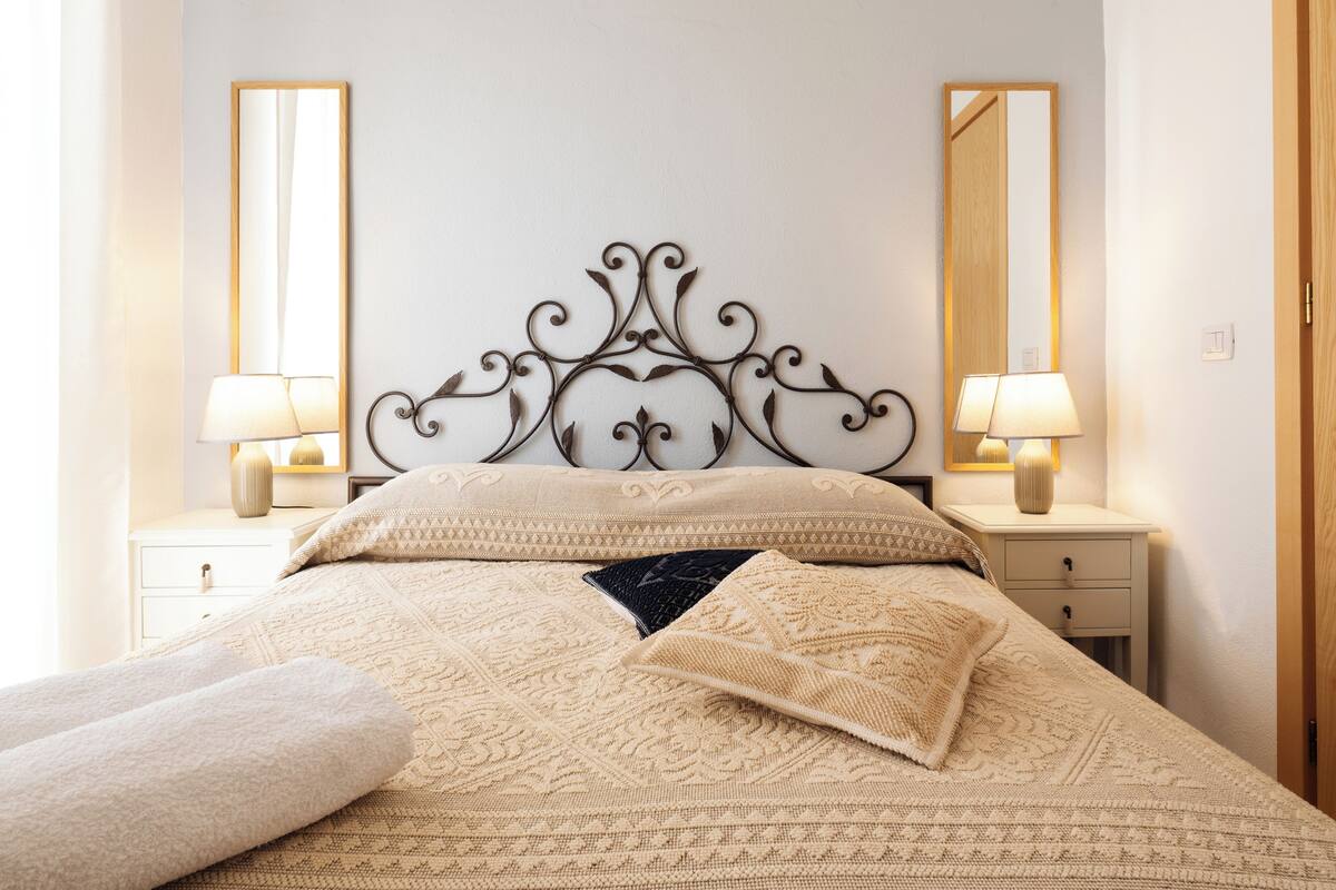 Una cama bien hecha con una colcha estampada, dos lámparas de noche y un cabecero decorativo.