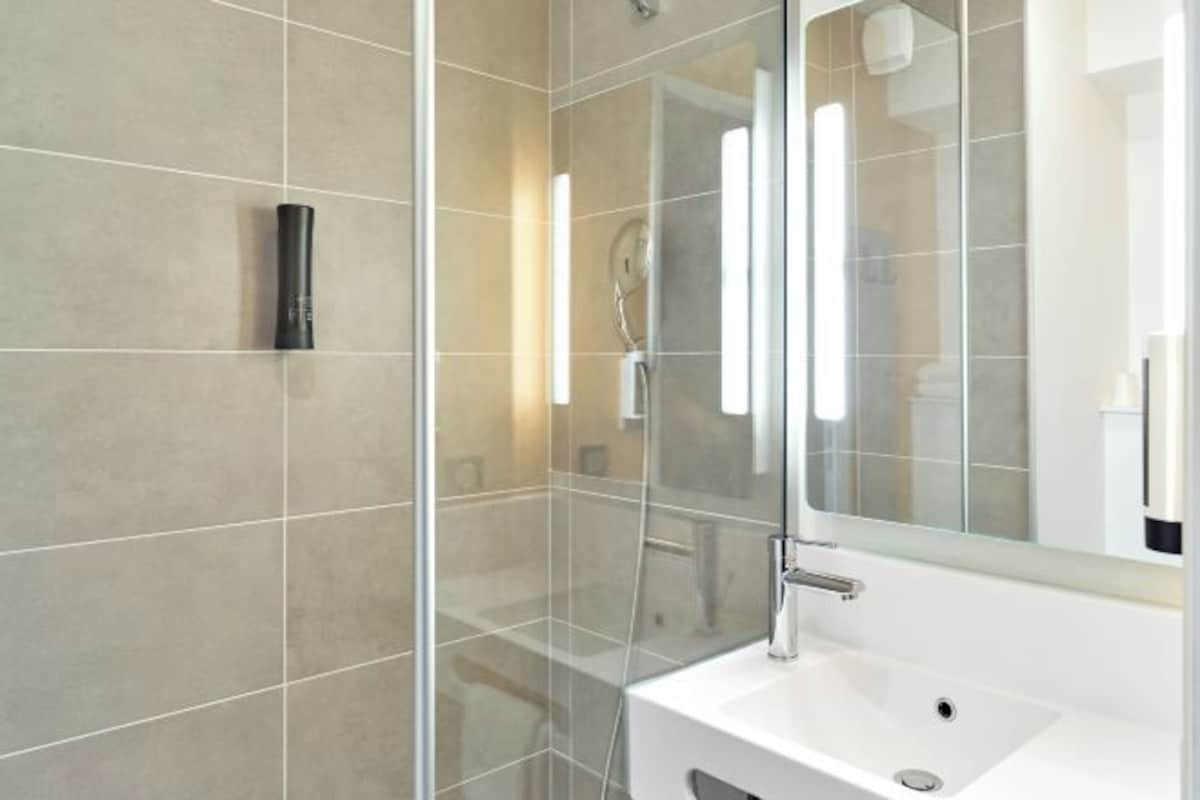 Ein modernes Badezimmer mit Duschkabine aus Glas, einem weißen Waschbecken und einem großen Spiegel.