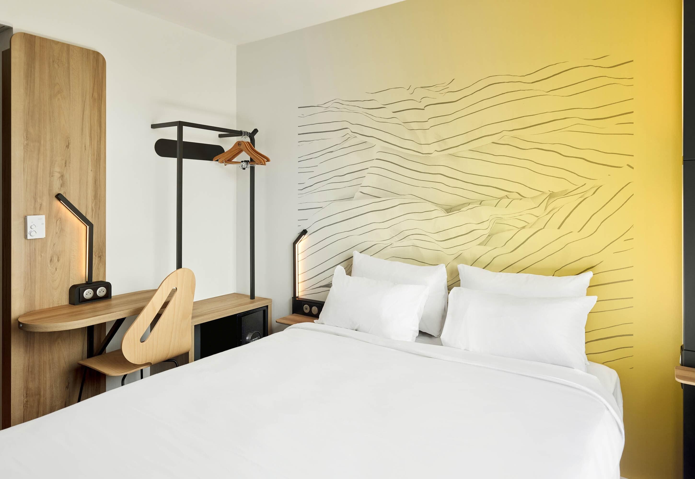 Una habitación de hotel moderna con una cama, un escritorio, una silla y un armario.