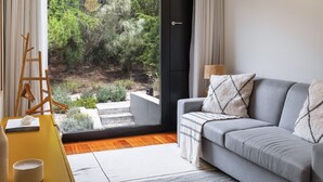 A modern living room with a grey sofa, a wooden ladder, and a view of a garden through a large sliding door. - Troia Beach House With Pool (Grandola)