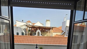 A balcony with a table and two chairs, overlooking a residential area with red-tiled roofs. - Historic Center Cascais Bolina 2 (Cascais)