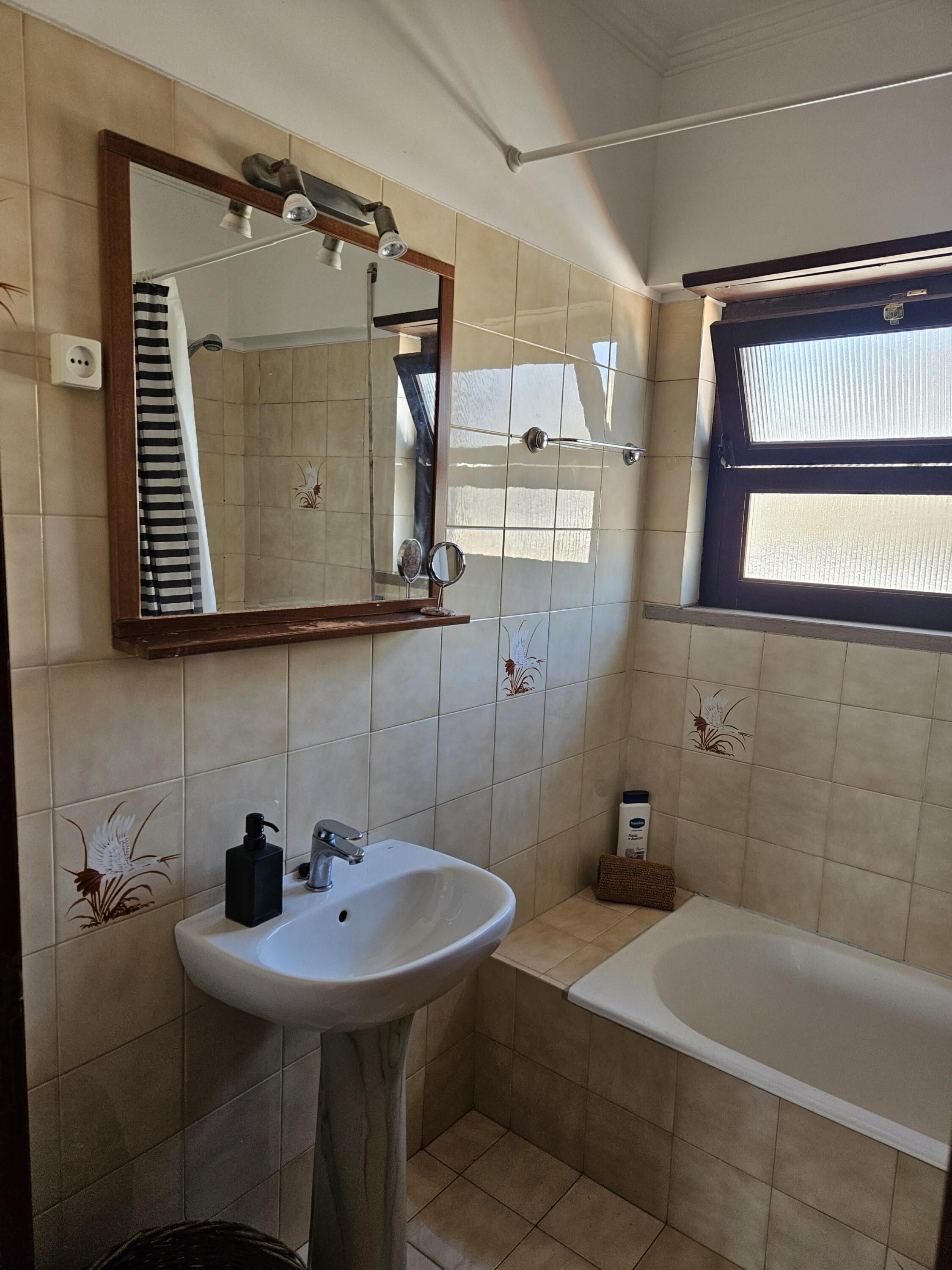 Ein Badezimmer mit Waschbecken, Spiegel und einem Fenster über der Badewanne.