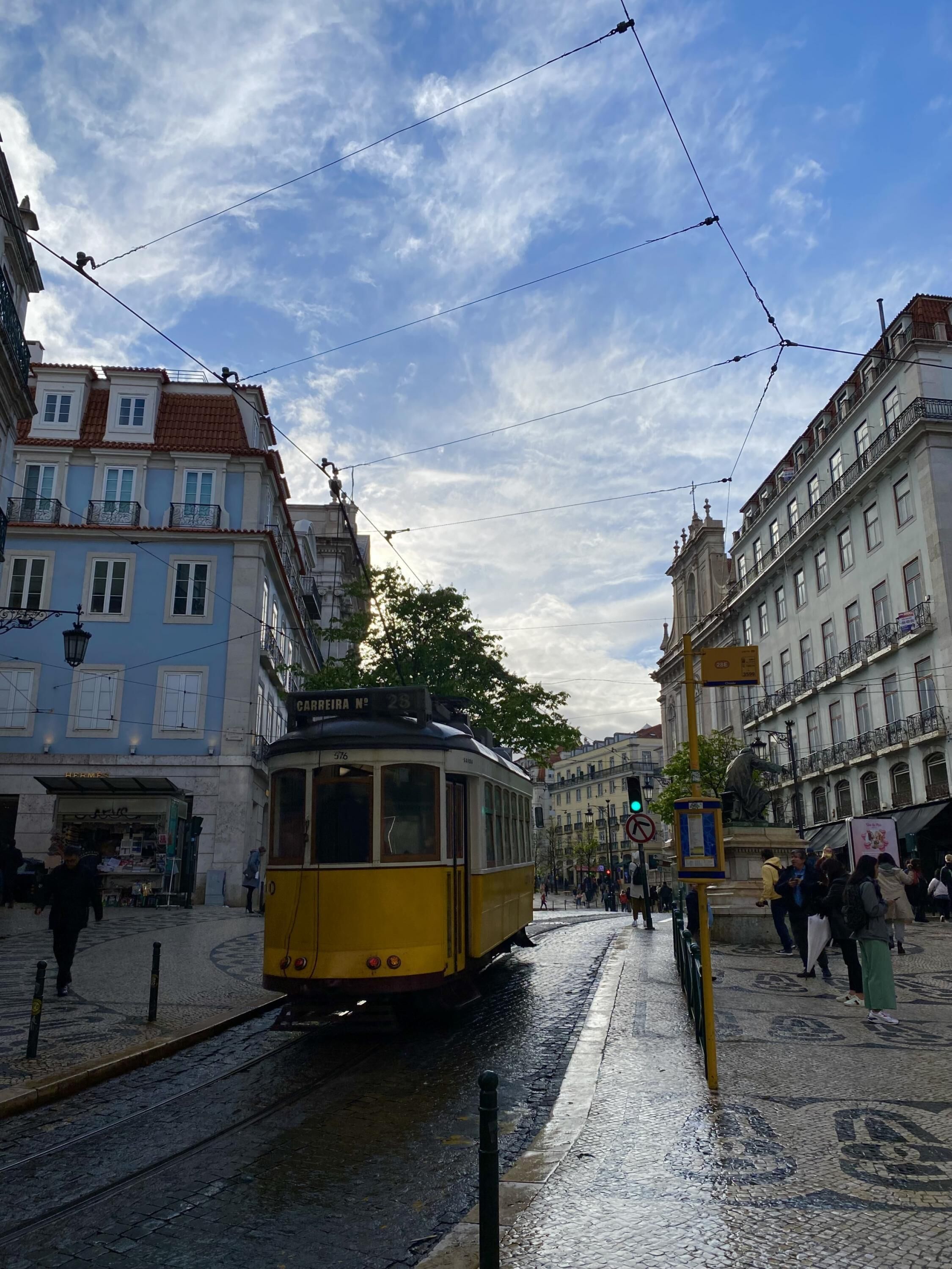 A tram on a cobblestone street in a European city, surrounded by historic buildings with balconies and a clear sky.