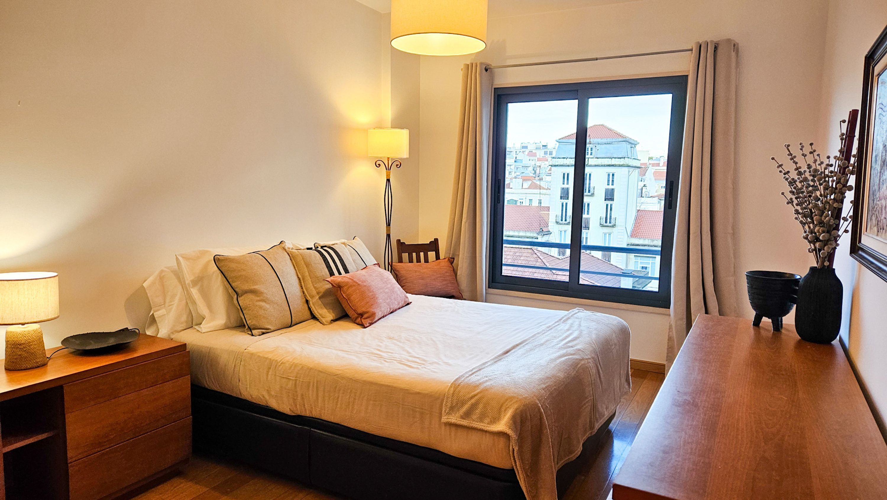 Une chambre d’hôtel avec un lit, une table de chevet, une lampe et une vue sur les bâtiments par la fenêtre.