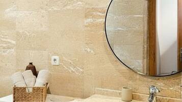 A bathroom with a marble wall, a round mirror, a sink, and a shelf with a basket and a bowl.