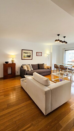 Una sala moderna con un sofá, una mesa de comedor con sillas y piso de madera.