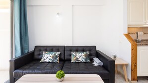 A modern living room with a black leather sofa, two patterned cushions, a small wooden side table, and a potted plant. - COSTA ADEJE BEACH & SUN 2 (Costa Adeje)