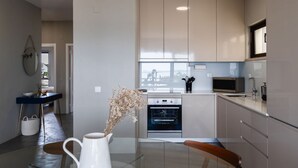 A modern kitchen with a glass table, a white pitcher, and a view of the city. - Soltroia Beach River Golf (Grandola)