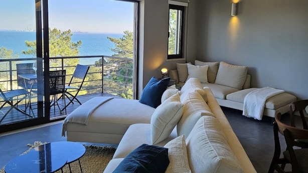 A modern living room with a large sofa, a small table, and a balcony with a view of the sea. - Soltroia Beach River Golf (Grandola)