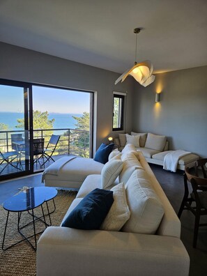A modern living room with a large sofa, a small table, and a balcony with a view of the sea. - Soltroia Beach River Golf (Grandola)
