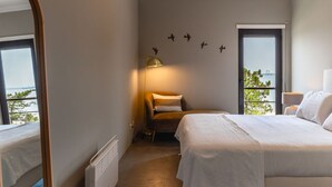 A hotel room with a large bed, a chair, a desk, a mirror, and a view of the sea. - Soltroia Beach River Golf (Grandola)