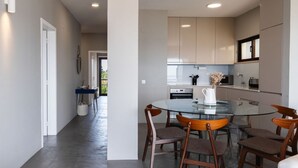 A modern kitchen with a glass dining table, wooden chairs, and a view of the outdoors. - Soltroia Beach River Golf (Grandola)