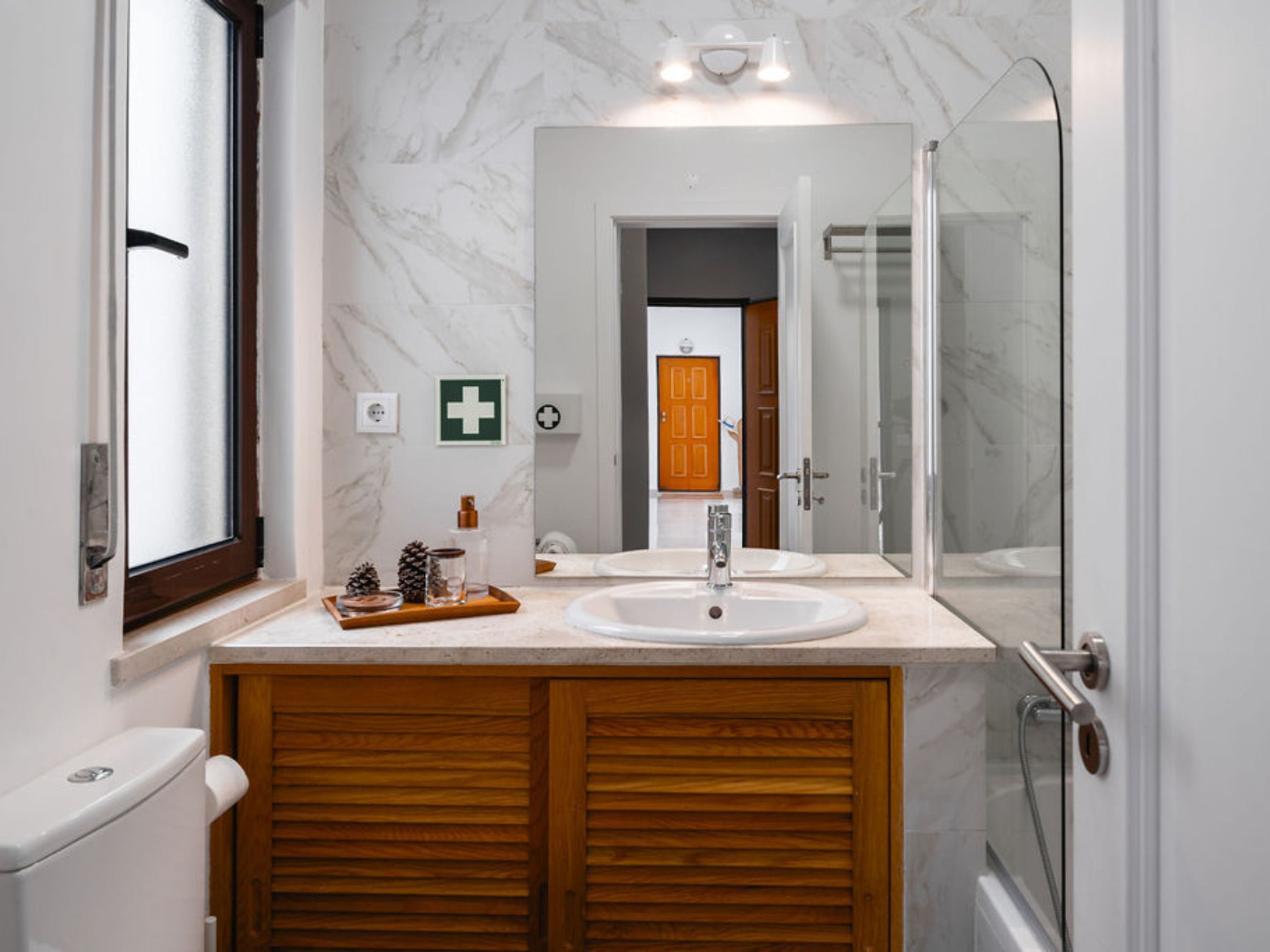 Une salle de bain avec un meuble-lavabo en bois, un lavabo blanc, un grand miroir et une cabine de douche en verre.