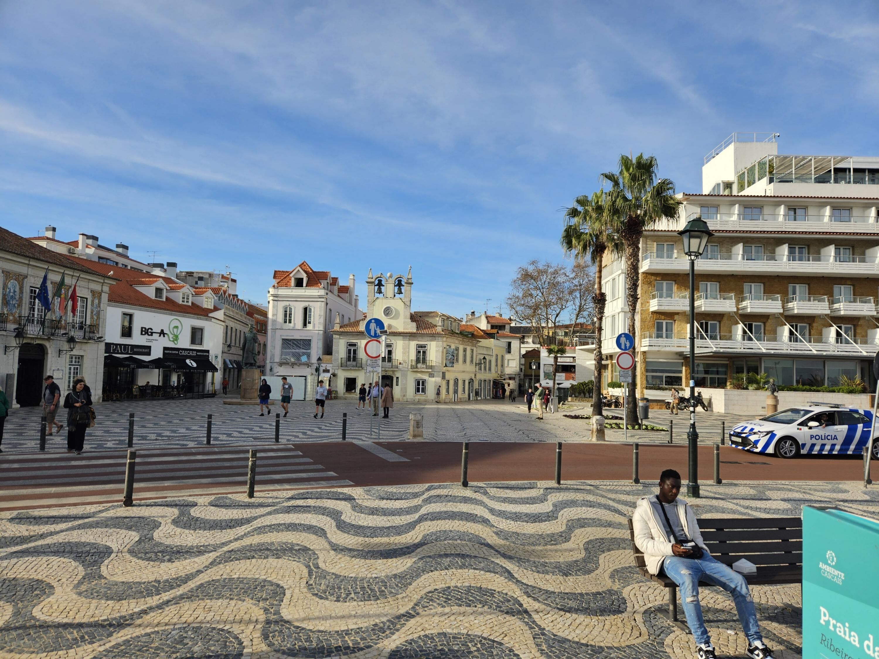 A plaza with cobblestone patterns, a bench, and a police car parked nearby.