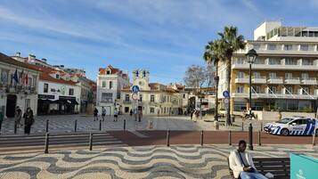 A plaza with cobblestone patterns, a bench, and a police car parked nearby.