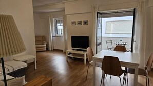 Een moderne woonkamer met een flatscreen televisie, een eettafel met stoelen, een bank en een raam met gordijnen.
