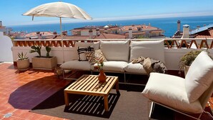 A terrace with a sofa, armchair, and table, overlooking a coastal cityscape. - Sunset Terrace Pool (Mafra)