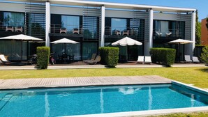 A modern hotel with a swimming pool, outdoor seating, and a well-maintained lawn. - Troia Beach Pool Golf Villa (Grandola)