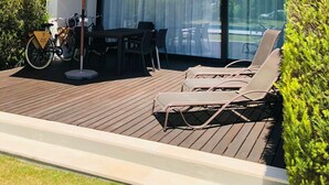 A modern outdoor patio with a table and chairs, a bicycle, and a lounge area with sun loungers. - Troia Beach Pool Golf Villa (Grandola)