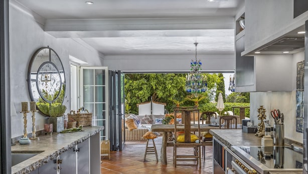 A modern kitchen with a large island, a dining area with outdoor seating, and a view of lush greenery. - Almancil Seaview Countrystyle Charm Villa (Loulé)