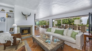 A spacious living room with a fireplace, a white sofa with green cushions, and a rustic coffee table. - Almancil Seaview Countrystyle Charm Villa (Loulé)