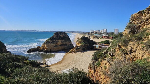 Eine Küstenlandschaft mit schroffen Klippen, einem Sandstrand und blauem Himmel.